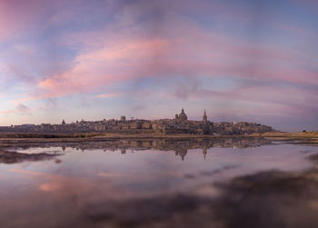 City by sea against cloudy sky during sunset