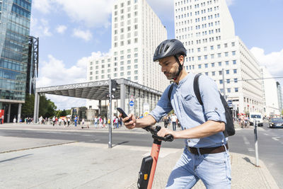 Businessman looking at the smartphone commuting on electric scooter in the city, berlin, germany