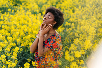 Smiling young woman standing by yellow flowering plants