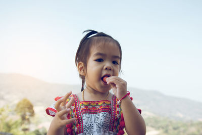 Portrait of cute girl eating strawberry against sky