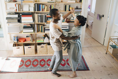 Smiling multiracial couple dancing together in living room at home