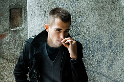 Young man smoking while sitting against wall