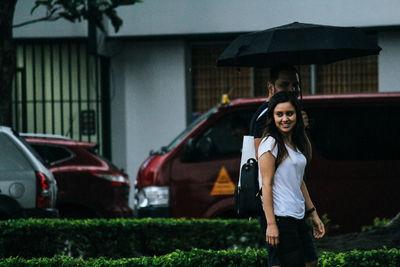 Portrait of woman standing by car against house