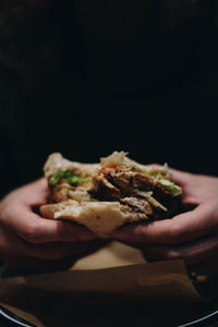 Cropped hands holding burger against black background