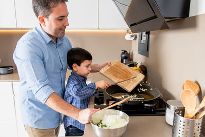 Side view cute concentrated boy stirring garlic on frying pan while learning to cook with father