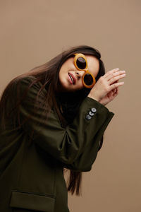 Portrait of young woman wearing sunglasses against brown background