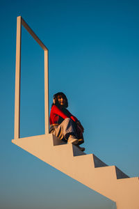 Low angle view of woman standing against clear blue sky