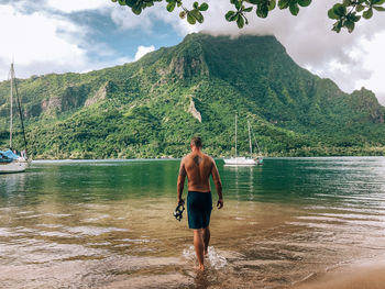 Rear view of shirtless man walking in sea