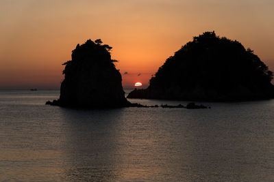Silhouette rock on sea against sky during sunset