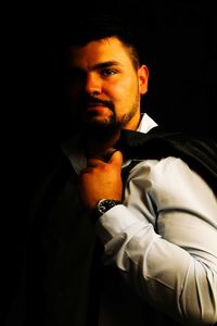 Portrait of young man standing against black background