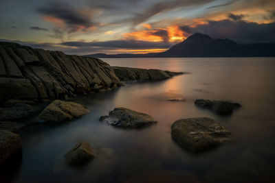 Rocks in sea against sky during sunset