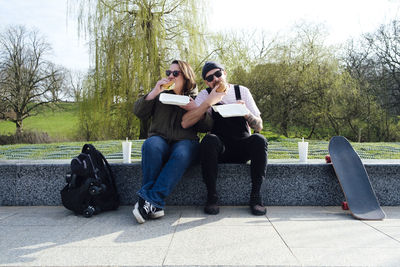 Friends eating burger by skateboard in park