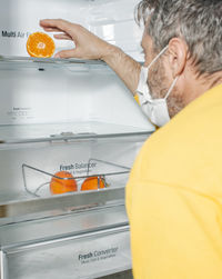 Middle-aged man with mask on his back looking at the empty fridge with half an orange