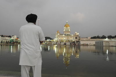 Rear view of man standing by lake against sky