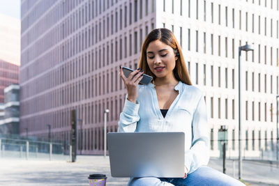 Smiling businesswoman using mobile phone sitting outdoors