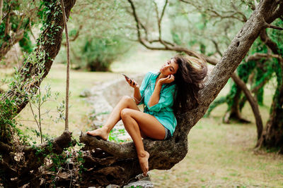 Young woman sitting on tree trunk in forest