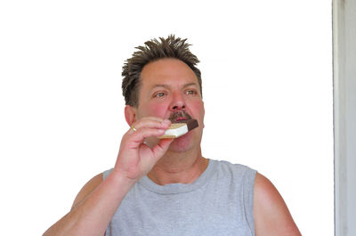Portrait of man eating ice cream against white background