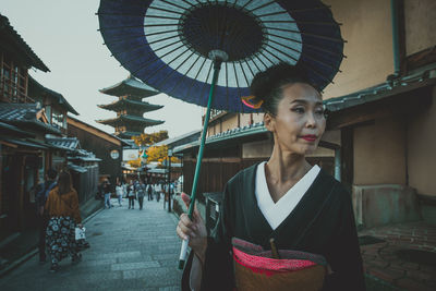 Portrait of woman with umbrella standing in city