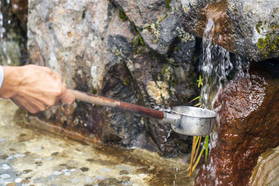 Cropped hand collecting water falling from rocks in container