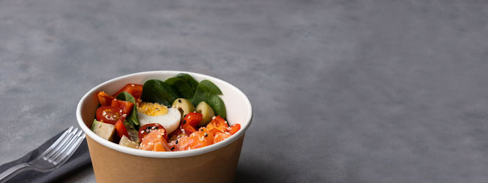 Takeaway poke bowl with fresh salmon, avocado, quinoa  in recycled kraft paper packaging. banner. 