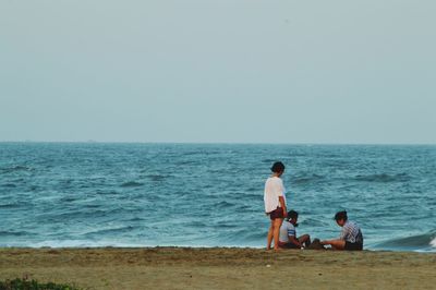 Parents with daughter making sandcastle at beach against clear sky