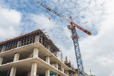 Low angle view of crane by building against sky