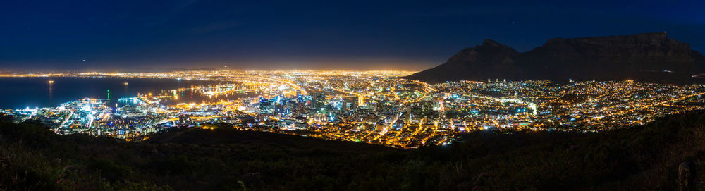 Illuminated city by sea against sky at night