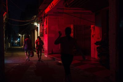 Rear view of people walking on illuminated street at night