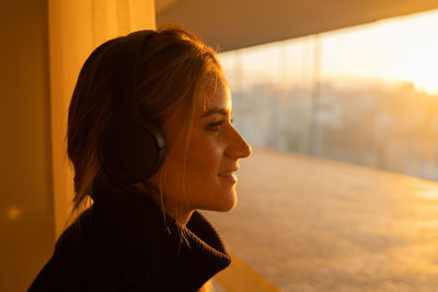 Woman listens to music with headphones by the window with a city view. mobile phone, technology, 