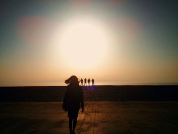 Woman standing on footpath at beach against sky during sunset