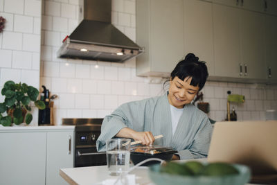 Smiling woman opening food container at table in kitchen