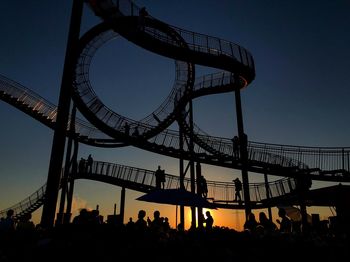 Silhouette people at amusement park against sky during sunset