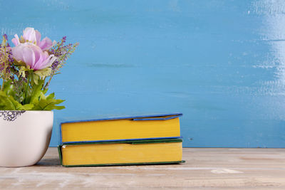 Pink flower vase on table against blue background with books. 