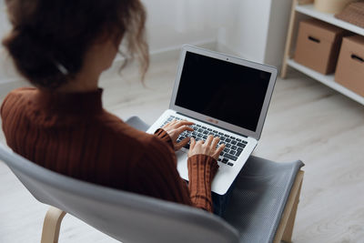 Rear view of woman using laptop at home