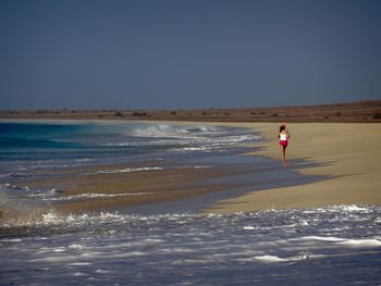 Full length of woman walking at beach against clear sky