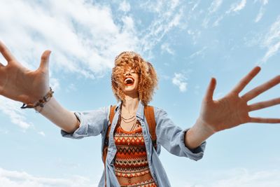 Side view of woman with arms raised standing against sky