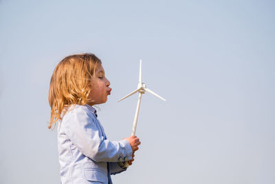 Side view of young woman holding umbrella against clear sky