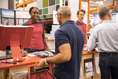 Male and female cashier talking with customers at checkout counter in hardware store