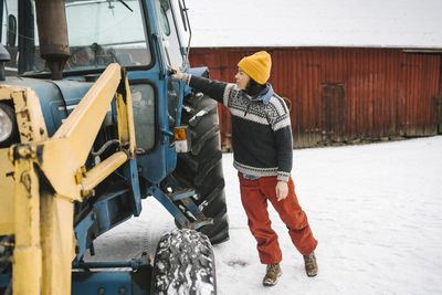 Full length of mature woman closing tractor's door during winter