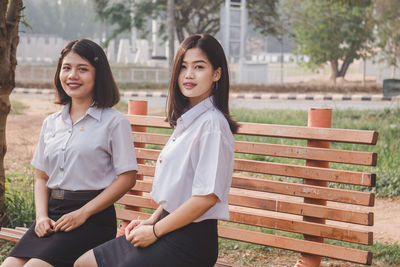 Portrait of smiling young woman sitting on bench in park