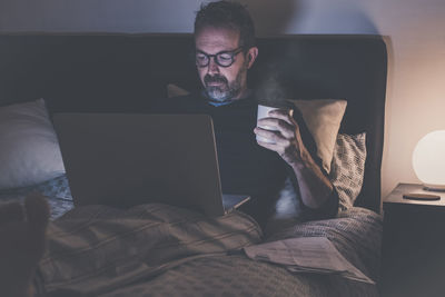 Man works with laptop lying on bed. male home working remote office. boy sit in bedroom use devices