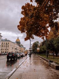 Wet street in city against sky during rainy season