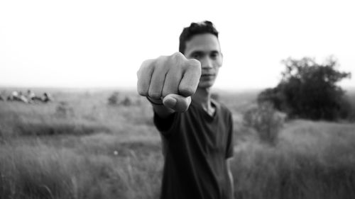 Portrait of young man clenching fist on grassy field against sky