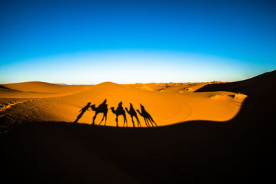 People on sand dune in desert against clear sky