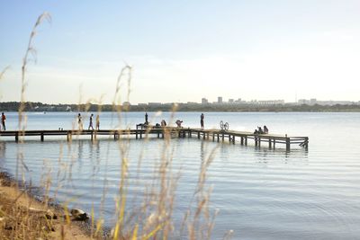 People on pier over lake against sky