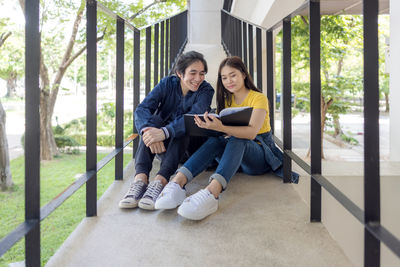 In the university campus, two asian couples sit on the stairwell with their thumbs up, working 