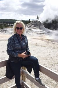 Smiling senior woman wearing sunglasses against old faithful geyser at yellowstone national park