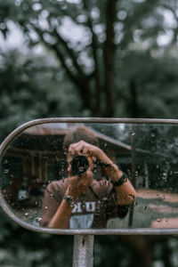 Reflection of woman photographing on wet windshield during rainy season