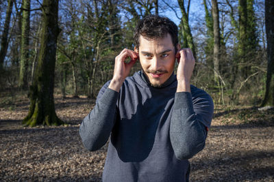 Runner listens to music while stretching in the woods.