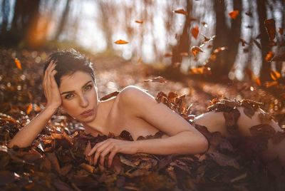 Portrait of naked young woman lying down amidst leaves on field